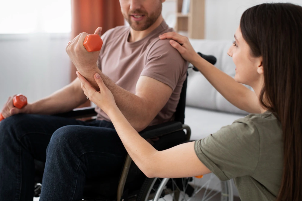 Physiotherapist guiding a Guillain-Barré Syndrome patient in a wheelchair using a resistance band during rehabilitation therapy.